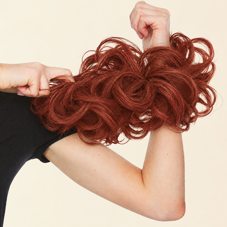 Hands stretching the JuvaBun Messy Bun in Copper Red to show the scrunchie band